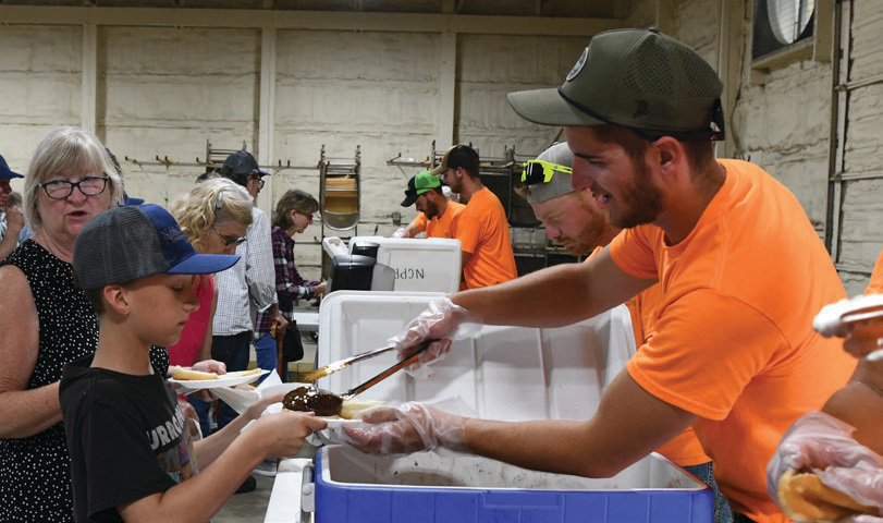 Right-of-Way Crew Member Jarrett Hawk serves a porkburger cooked by the Noble County Pork Producers to one of our younger visitors.