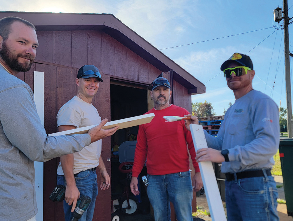 Employees Cody Kirkpatrick, Zane Gray, Rob Hauck, and Luke Gillis cut and paint new trim for Trinity Daycare Ministry’s renovated shed.